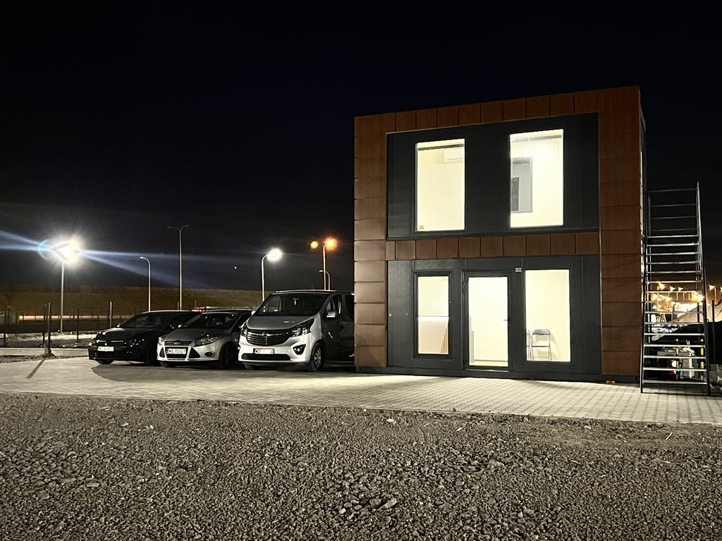 Oświetlone biuro Skyway Parking przy lotnisku Chopina nocą – całodobowa obsługa parkingu, bezpieczny punkt odbioru i transferu pasażerów 24/7 na Okęciu.