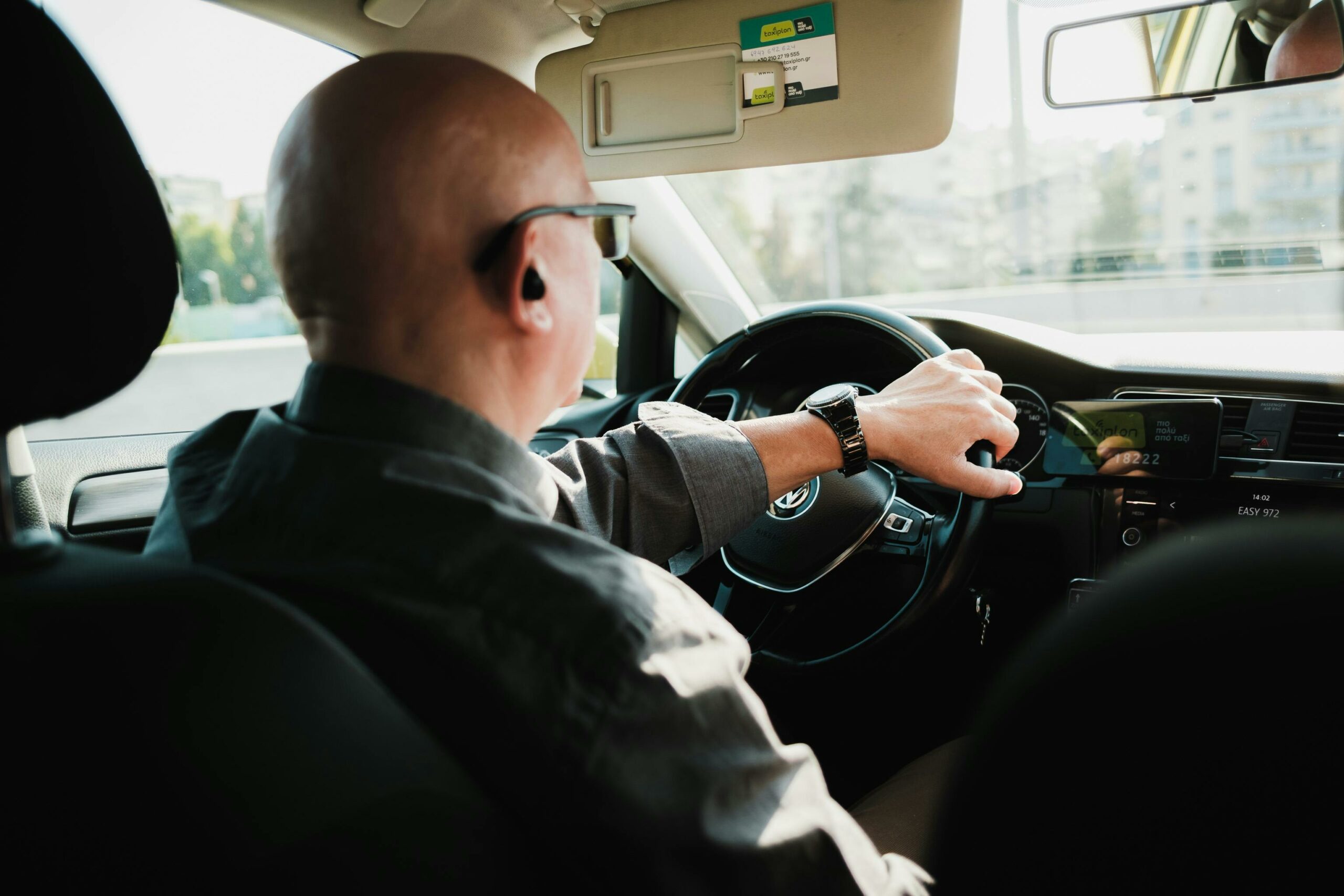 services-01 Bald man driving in a car, urban setting, viewed from behind.